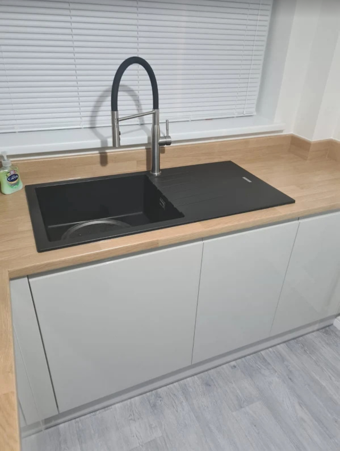 Black composite kitchen sink with a modern pull-out mixer tap installed in an oak worktop