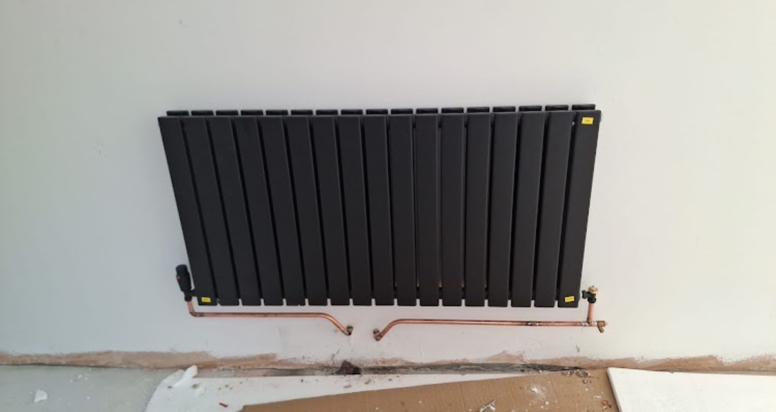 Black flat-panel designer radiator fitted to a wall with new copper pipework and valves