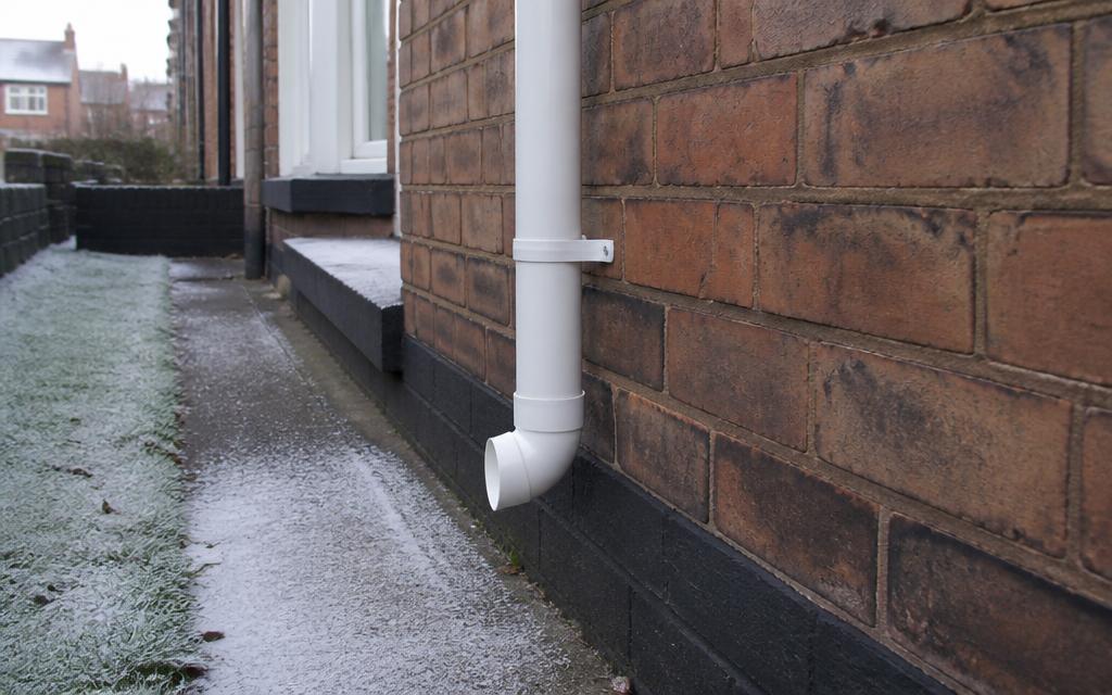 External white condensate pipe on a house wall during frosty winter weather
